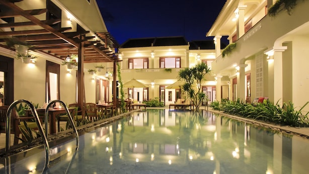A well-lit swimming pool with a reflection of the surrounding buildings and furniture. - Green Boutique Villa (Da Nang)