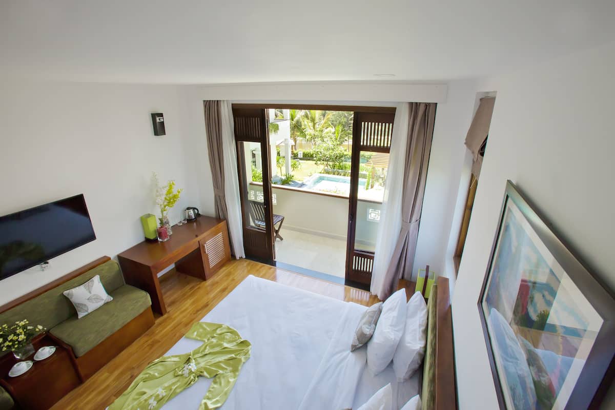 Une chambre d’hôtel équipée d’un lit, d’une télévision, d’un canapé, d’un bureau et d’un balcon donnant sur un paysage verdoyant.
