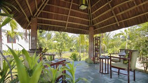 A covered outdoor seating area with brick pillars, wooden furniture, and lush greenery in the background. - Green Boutique Villa (Da Nang)