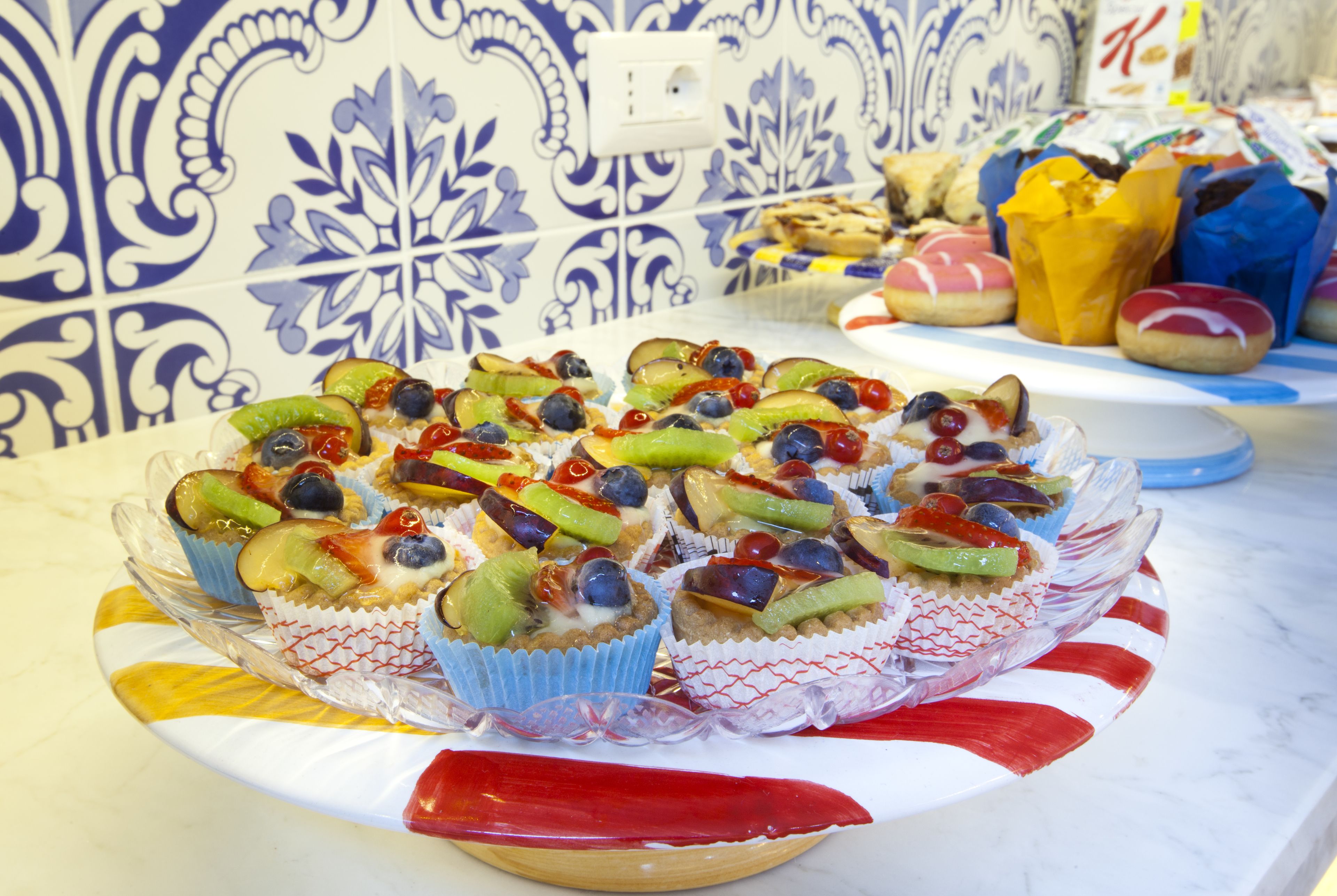 A table with a variety of pastries and desserts, including cupcakes with fruit toppings, arranged on a decorative plate.