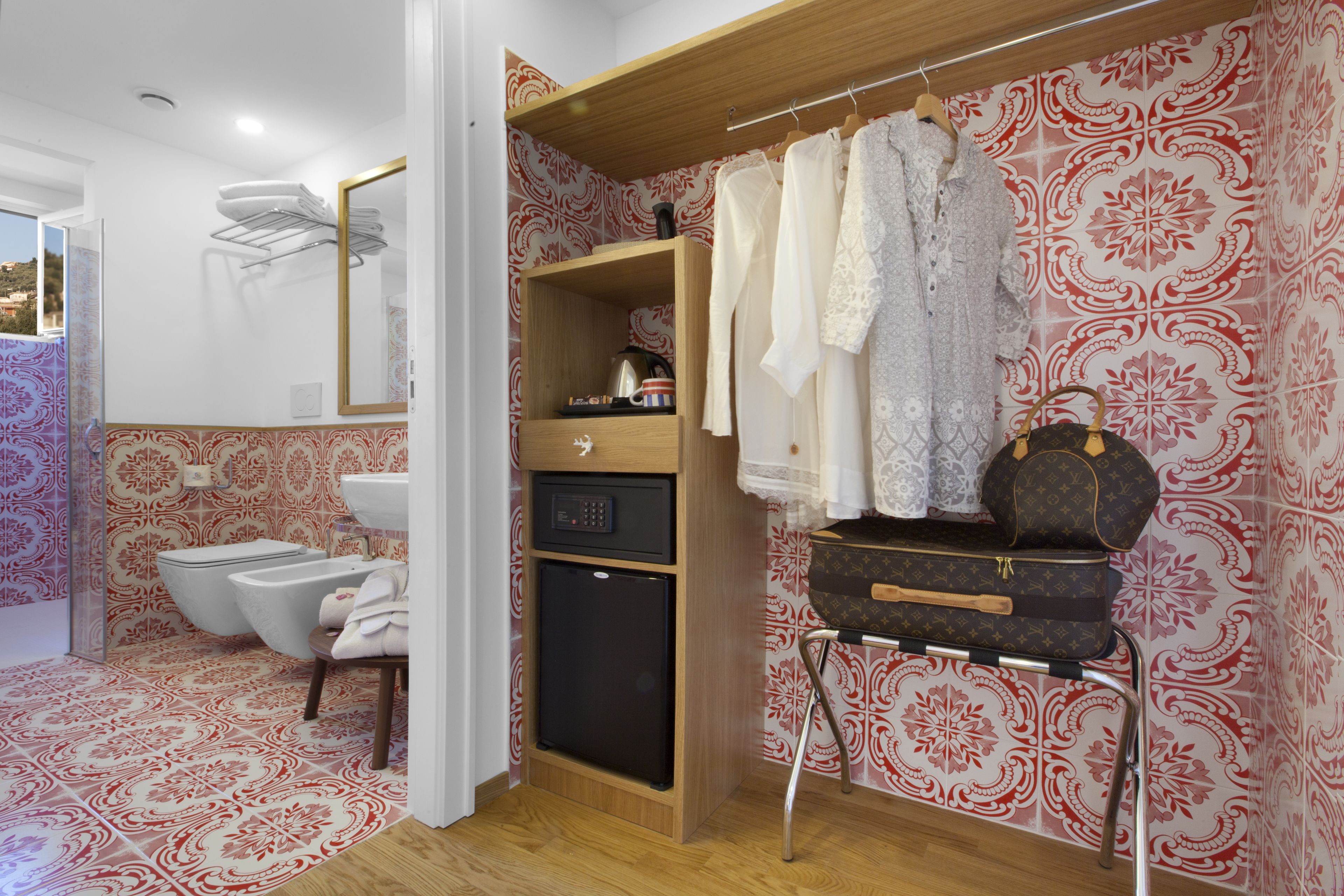 A bathroom with a toilet, sink, and shower. There is a wooden cabinet with towels and a suitcase on a stand.