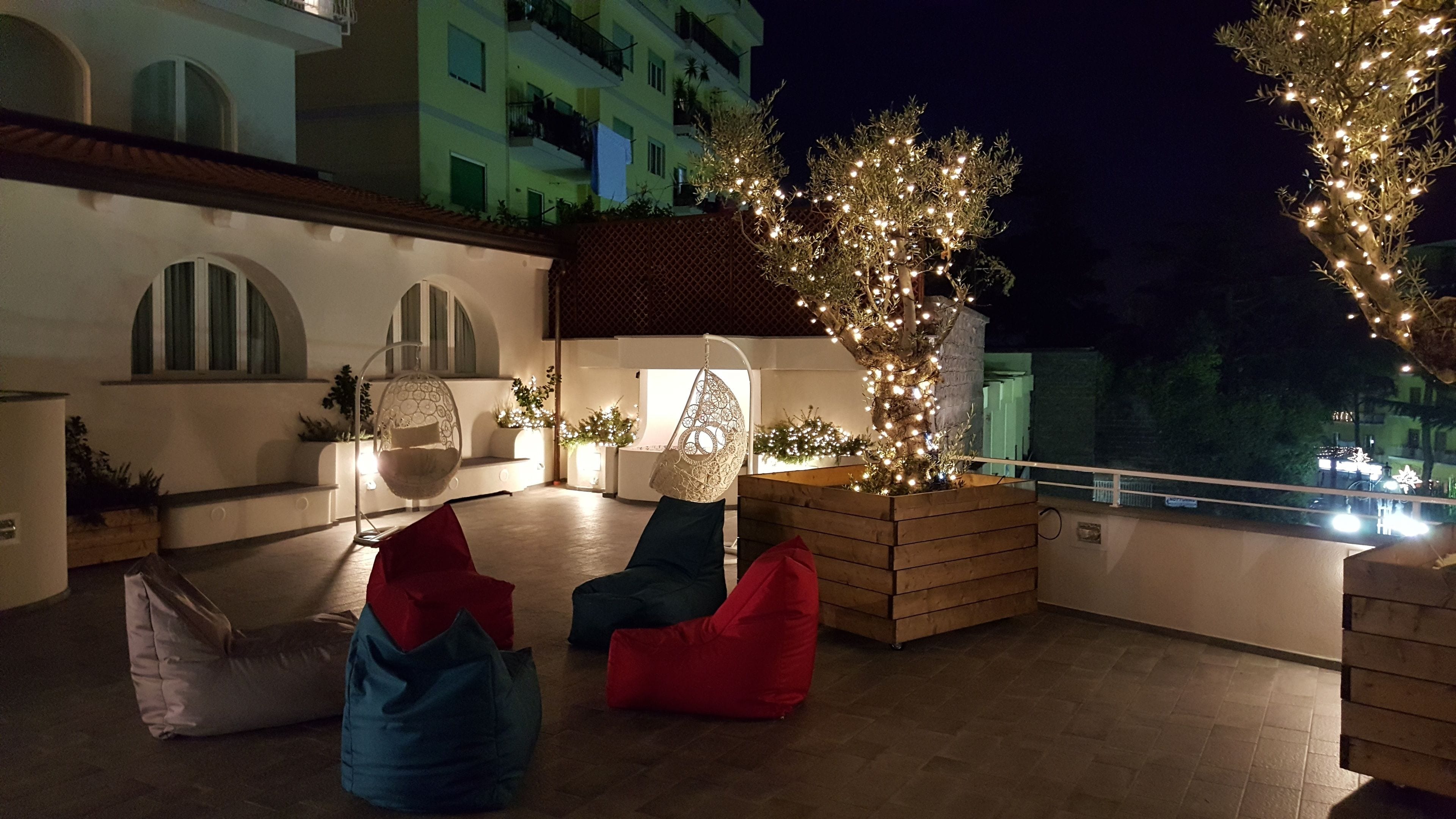 A rooftop terrace with seating areas, a decorative tree, and a view of a building with balconies.