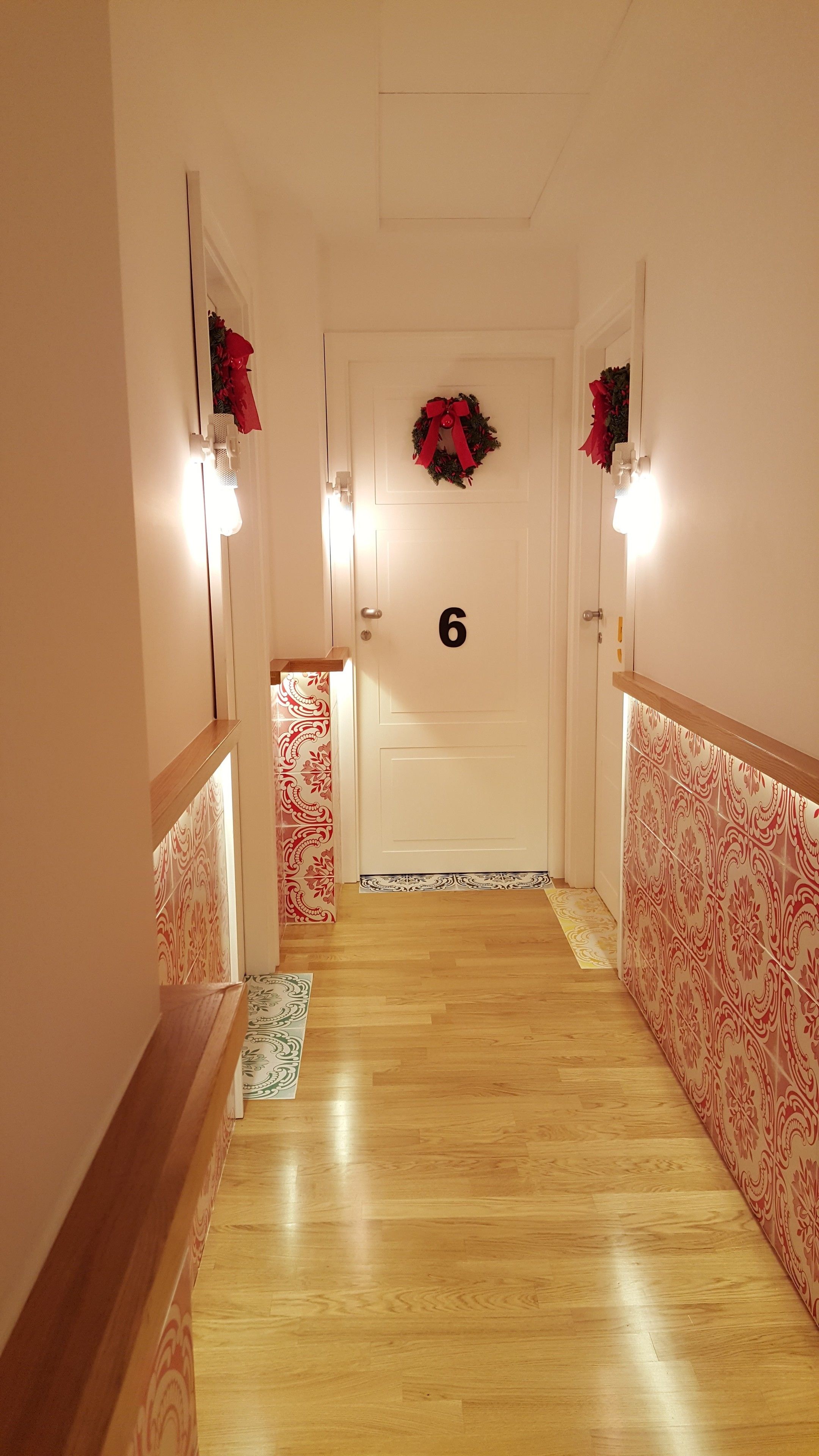 Un couloir doté d’un plancher en bois, d’une porte numérotée 6 et de murs recouverts d’un papier peint à motifs.