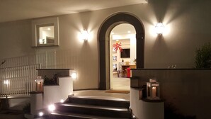 A staircase leading to a door with a glass panel, flanked by wall-mounted lights and a small plant. - Maison Kalea (Sorrento)