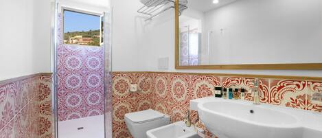 A bathroom with patterned tiles, a sink, a mirror, and a shower.