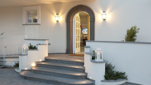 A set of stone steps leading to a white door with an arched entrance, flanked by wall-mounted lights and small planters. - Maison Kalea (Sorrento)