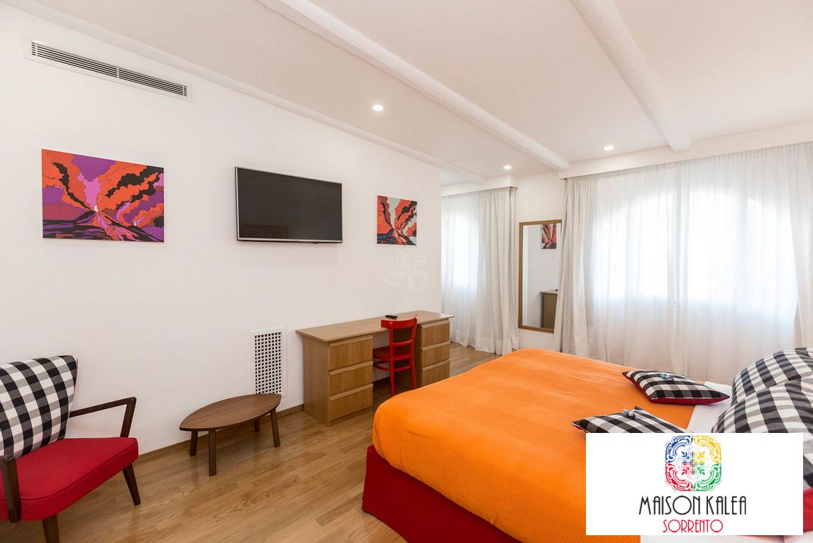 A hotel room with a bed, a desk, a chair, and artwork on the walls.