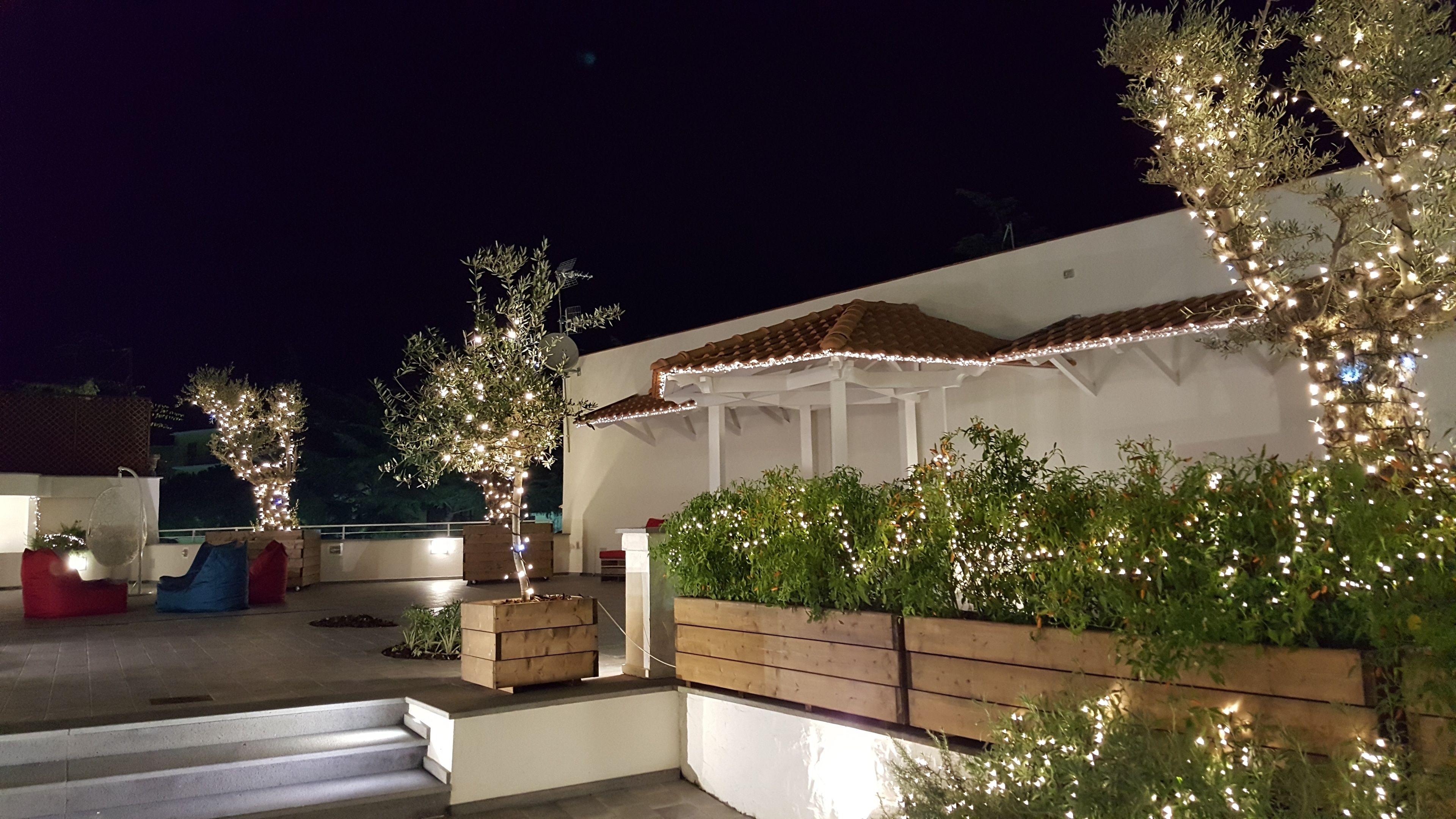 Une terrasse sur le toit agrémentée d’une pergola, de guirlandes lumineuses et de jardinières en bois remplies de verdure.
