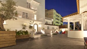 A courtyard with a wooden bench, a small garden, and a building with balconies and outdoor seating. - Maison Kalea (Sorrento)