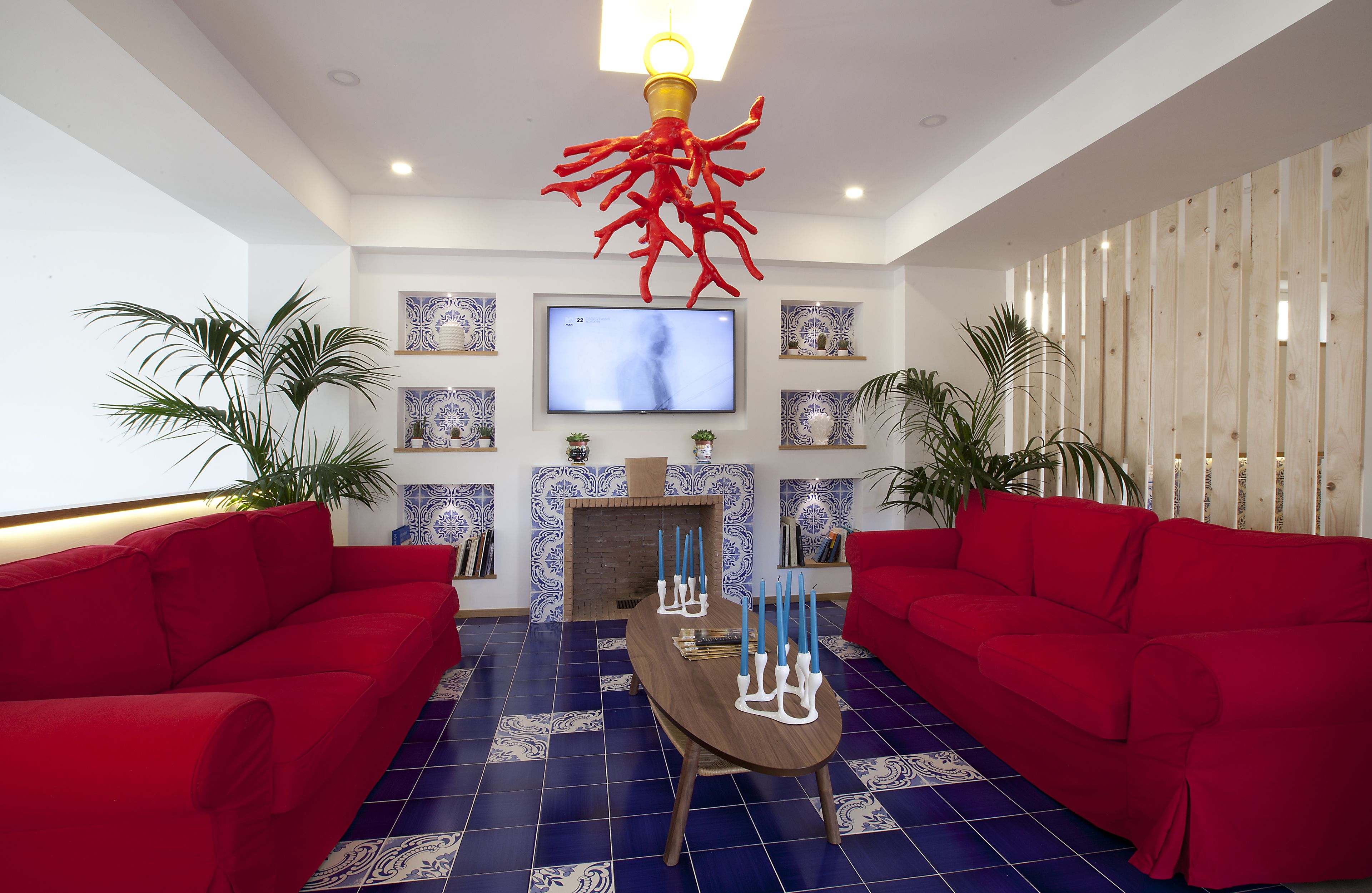 A modern living room with red sofas, a wooden coffee table, and decorative elements like a red coral sculpture and blue patterned tiles.