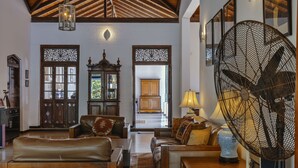 A spacious living room with leather sofas, a wooden coffee table, and a large fan. There is a wooden cabinet and a decorative vase on a side table. - Villa Republic River View Bentota (Aluthgama)