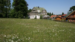 A large hotel with multiple stories and a green roof, surrounded by a grassy field with white flowers.