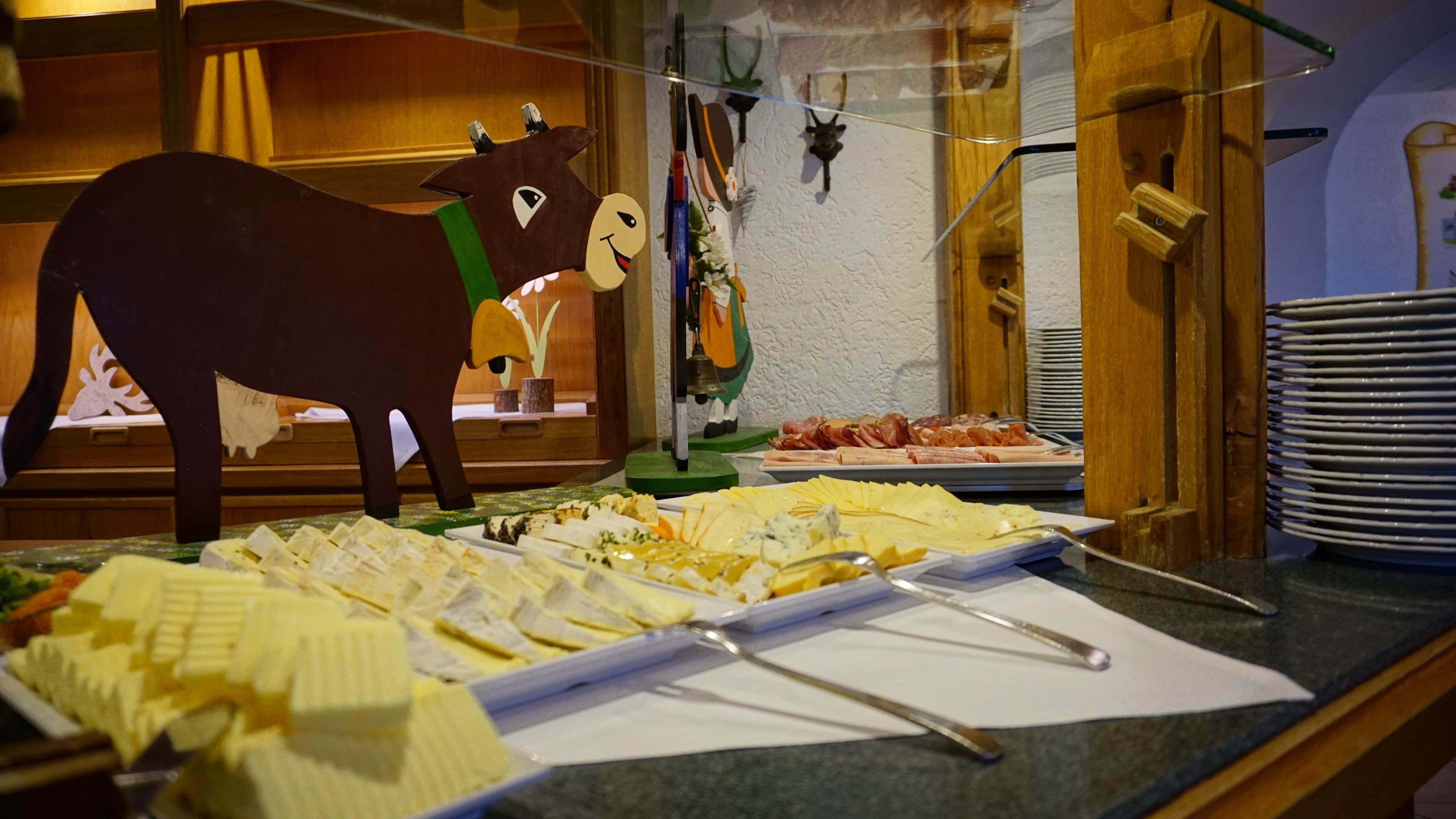 A buffet area with various cheeses and meats, a wooden cow decoration, and a bell on a stand.