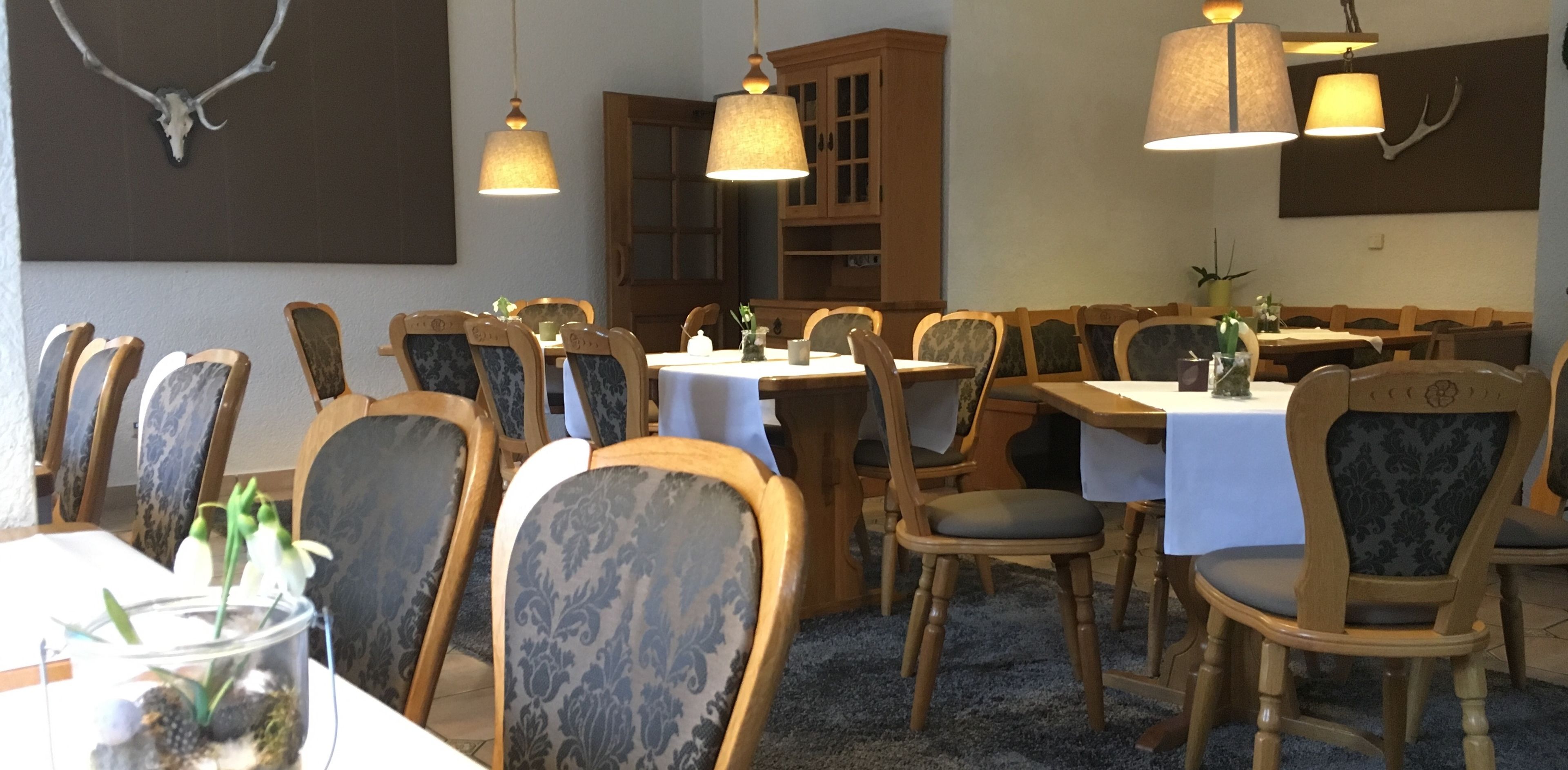 A dining area with wooden tables and chairs, pendant lights, and wall-mounted decor.