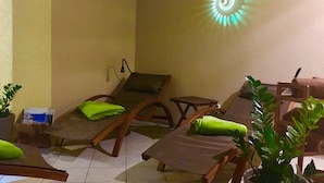 A room with two wooden lounge chairs, a small table, and a wall-mounted lamp.