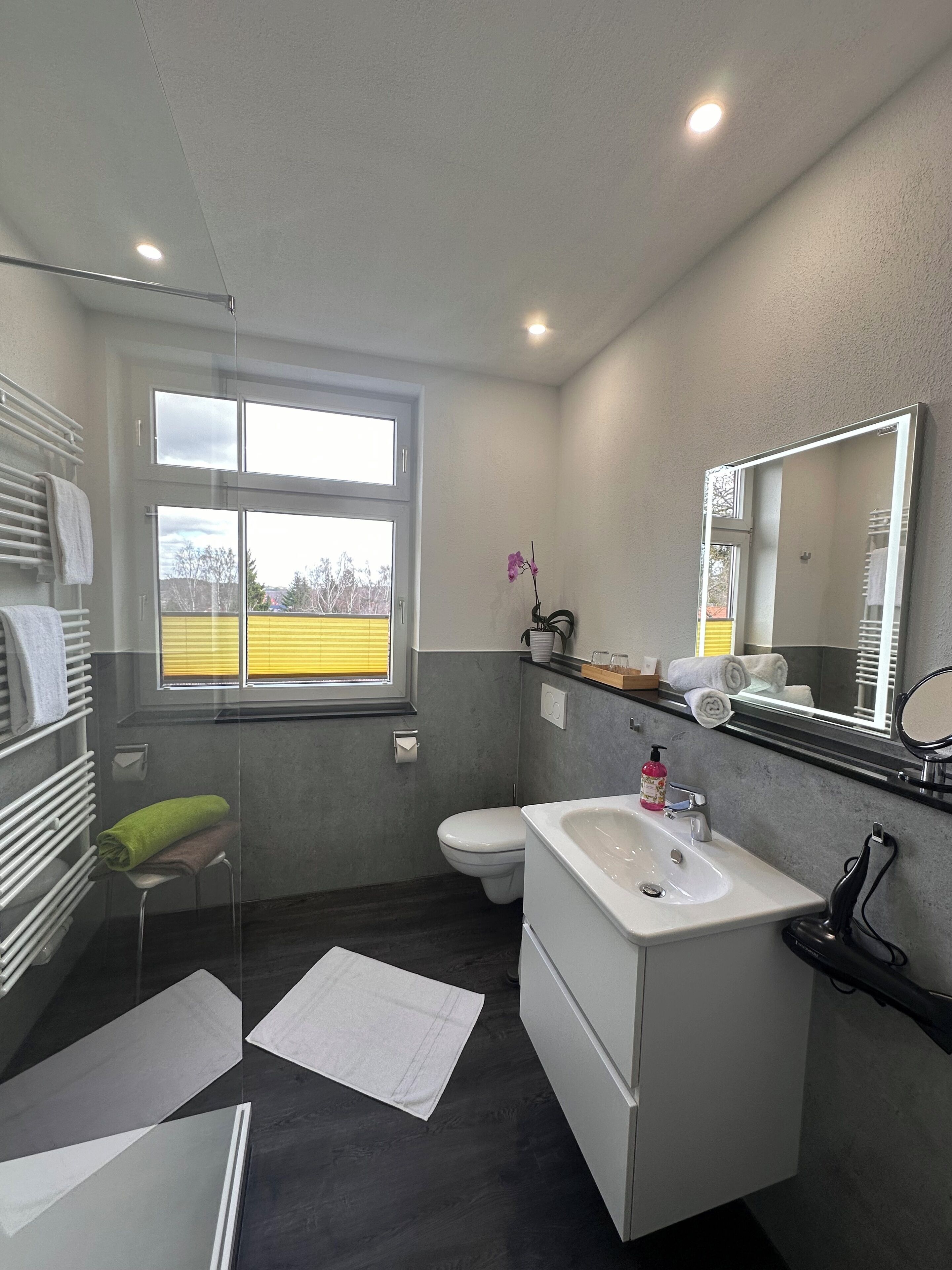 Un baño moderno con bañera, inodoro y lavamanos. Hay una ventana que proporciona luz natural y vistas al exterior.