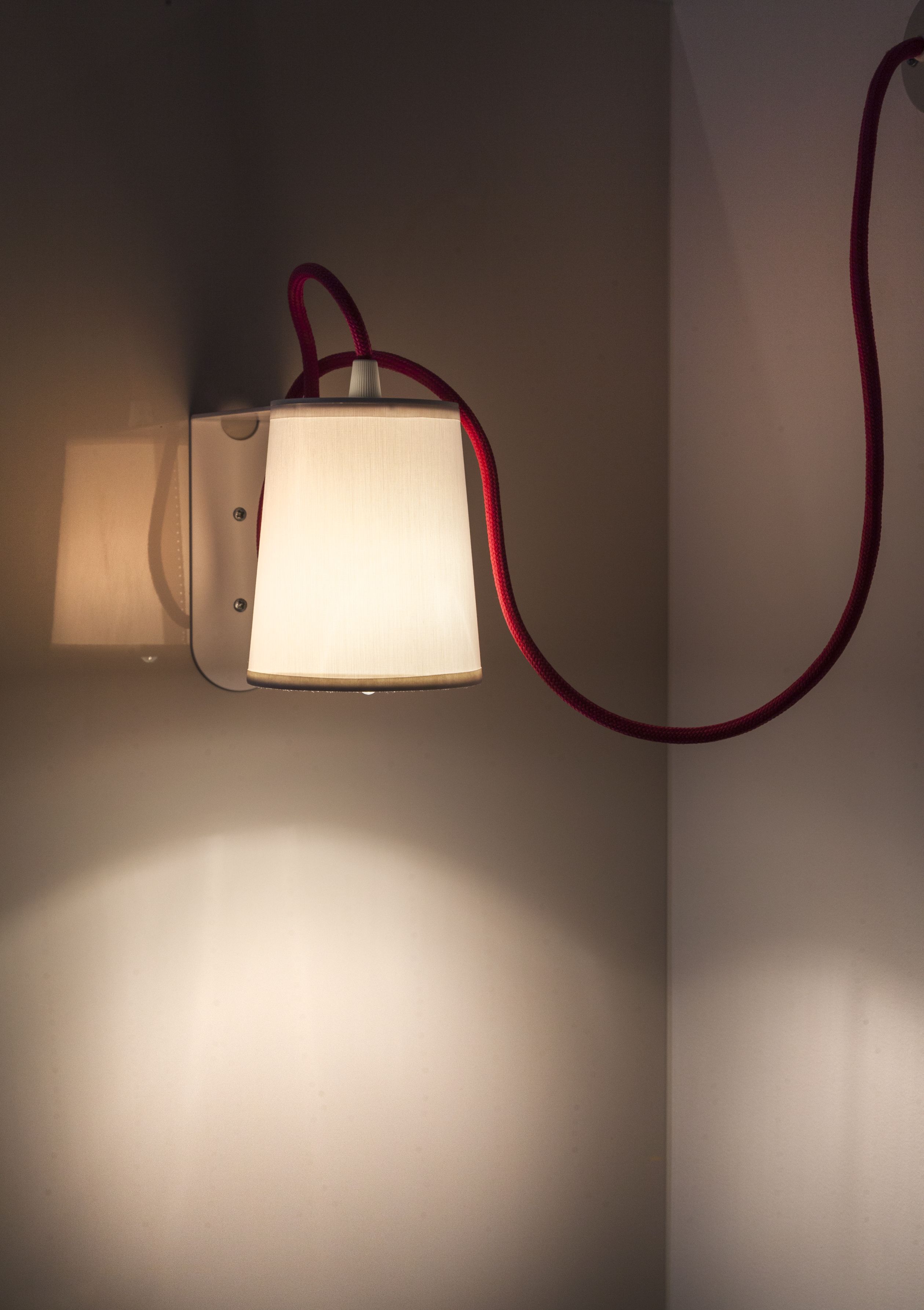 A wall-mounted lamp with a white shade and a red cord.