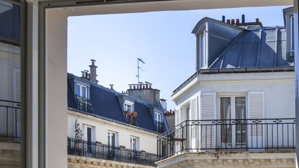 A view of a multi-story building with balconies and shutters, viewed from a balcony with a wooden railing. - Hôtel Le Mireille (Paris)
