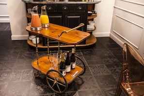 A wooden cart with bottles and glasses, a juice dispenser, and a wine bottle in a kitchen setting. - Hôtel Le Mireille (Paris)