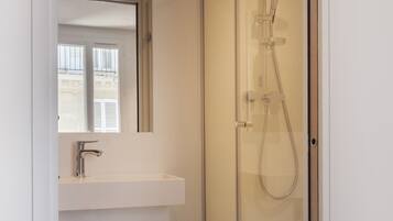 A modern bathroom with a glass-enclosed shower, a white sink, and a mirror above it.