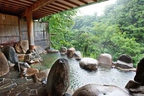 A traditional Japanese onsen with large rocks, a wooden structure, and lush greenery in the background. - Hotel New Ohruri (Nikko)