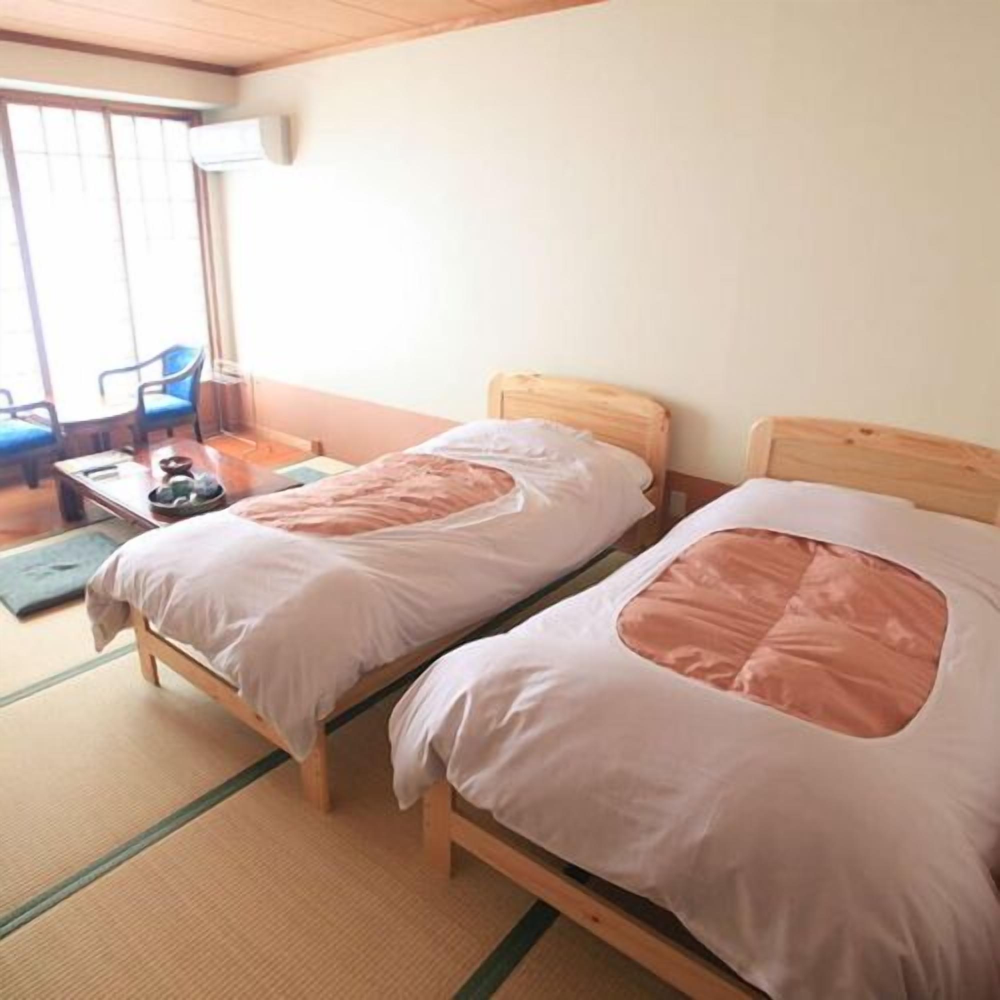 A room with two wooden beds, a small table, and a chair.