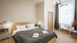 A modern hotel room with a large bed, bedside lamps, a small table, and a chair. - Bearsleys Downtown Apartments (Riga)