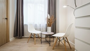 A modern room with a wooden floor, two white chairs, a small round table, a vase with dried plants, and a lamp. - Bearsleys Downtown Apartments (Riga)