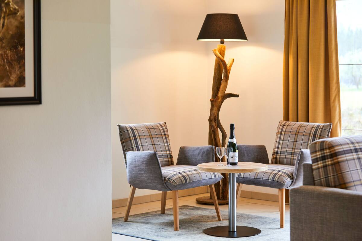 A modern living room with a round table, two grey upholstered chairs, a floor lamp, and a bottle of wine.