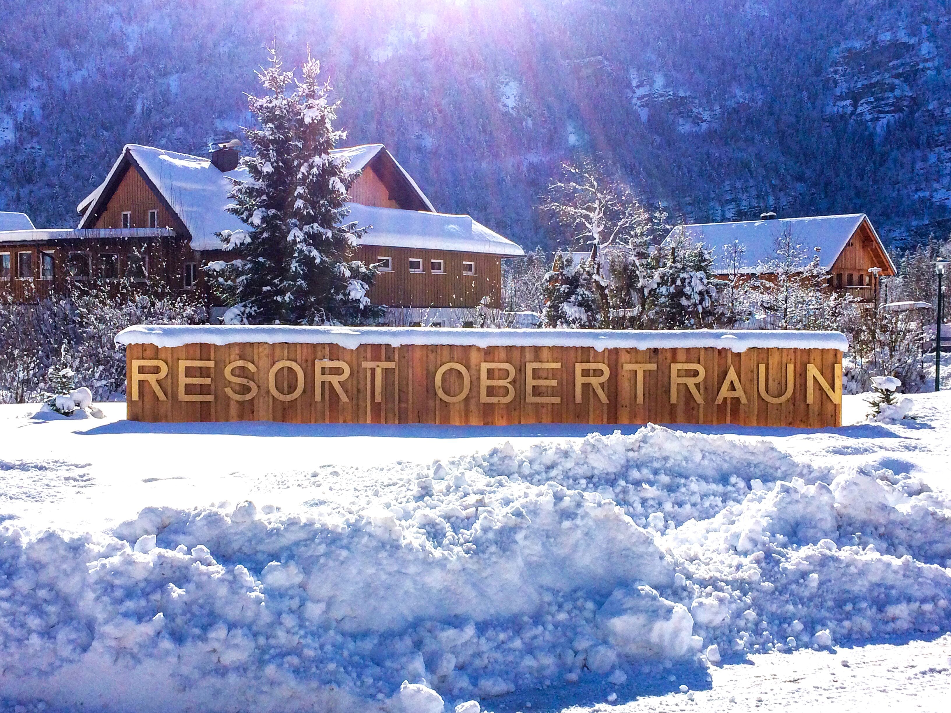 A wooden sign with "RESORT OBERTRAUN" carved in it, surrounded by snow and trees.