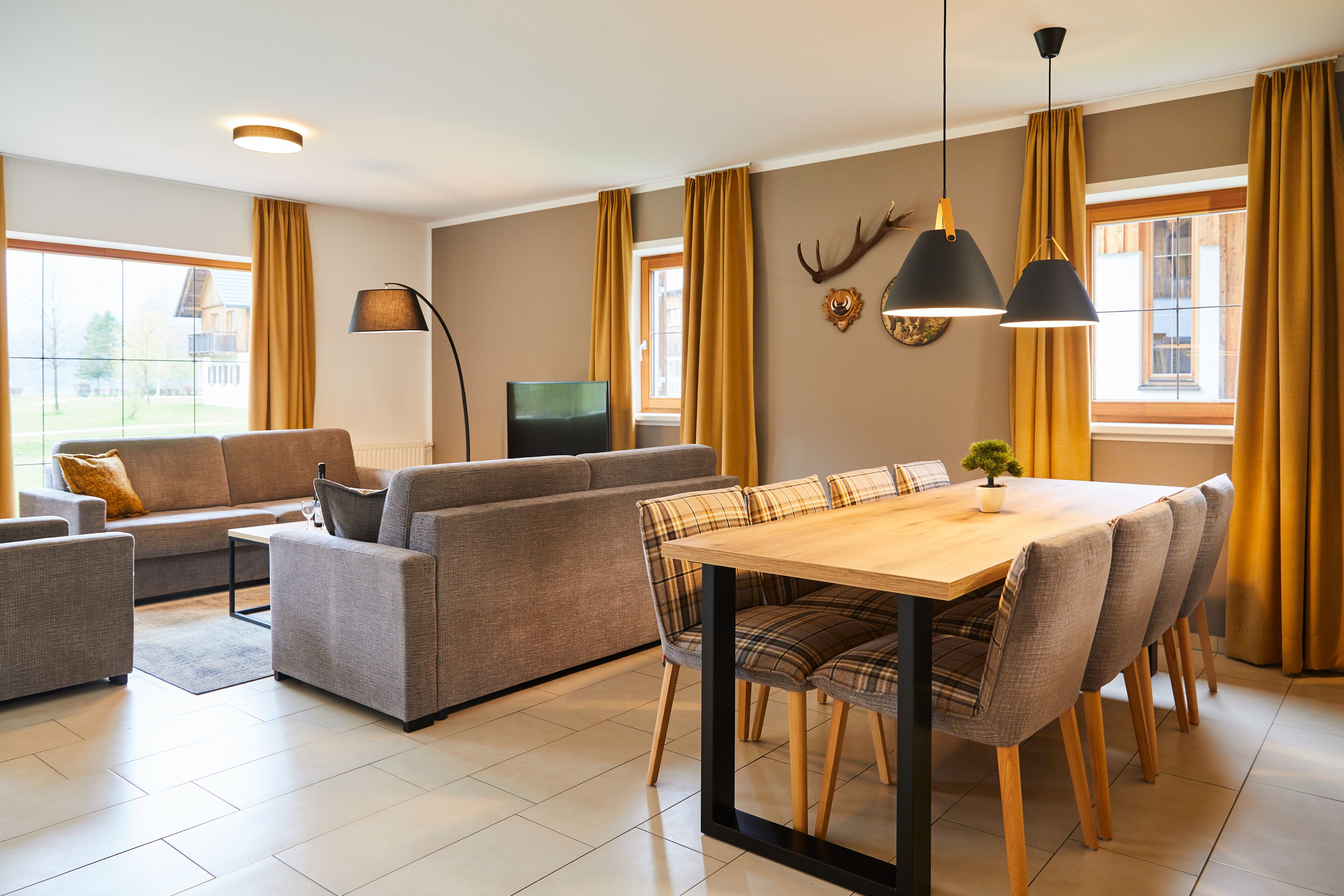 Ein modernes Wohnzimmer mit einer Couch, einem Esstisch mit Stühlen, einem Fernseher und einem großen Fenster mit Vorhängen.