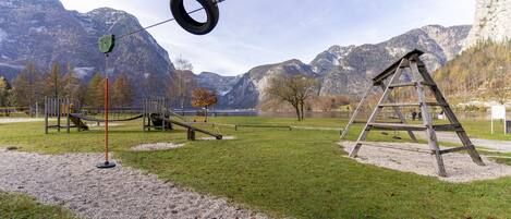 A playground with swings, a tire swing, and a climbing structure in a park with mountains in the background.