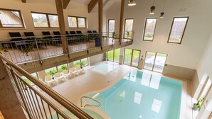 A large indoor swimming pool with a balcony above, wooden beams, and large windows. - Dormio Resort Obertraun (Obertraun)