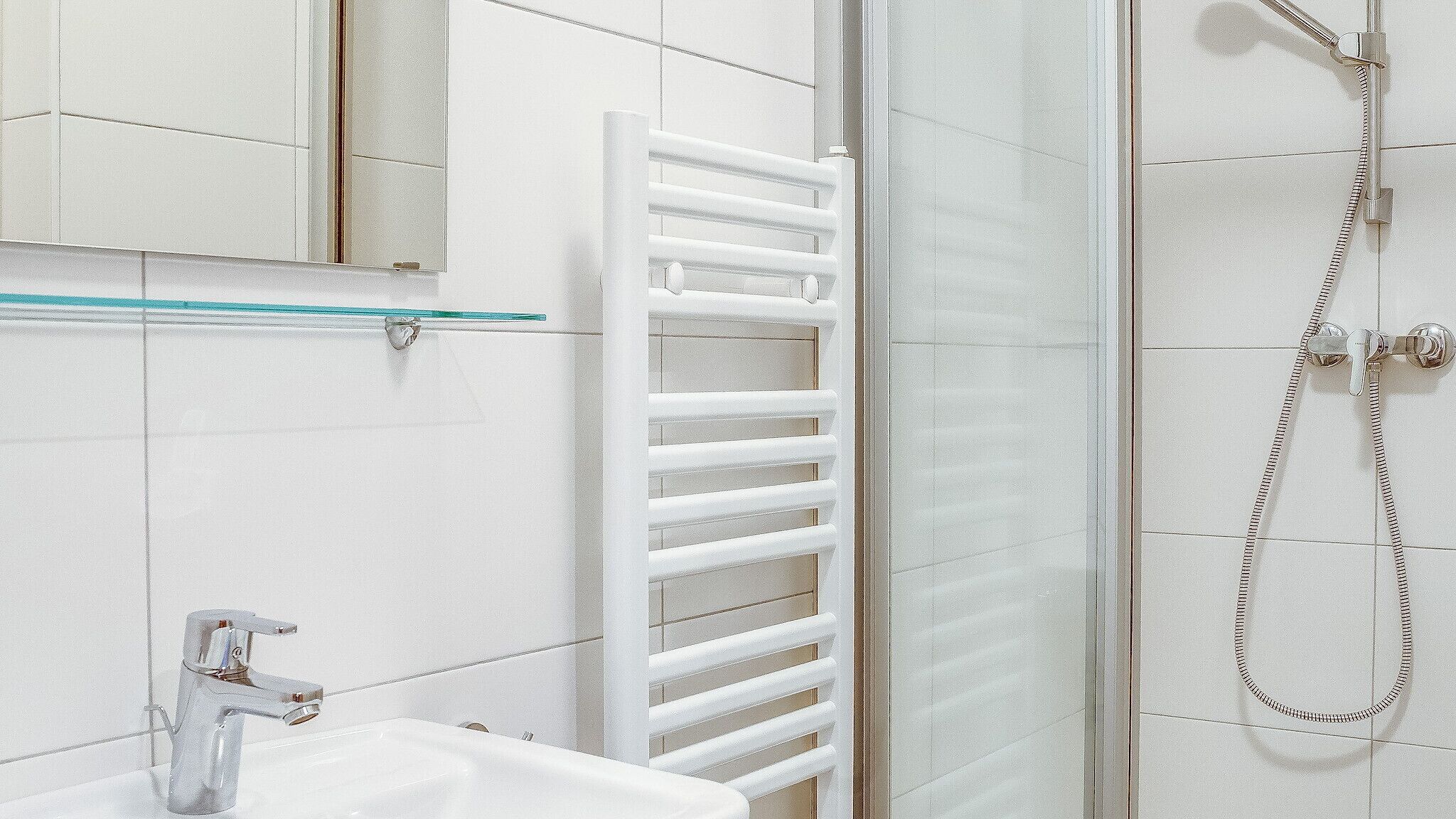Une salle de bain avec un lavabo blanc, une cabine de douche en verre et un porte-serviettes blanc.