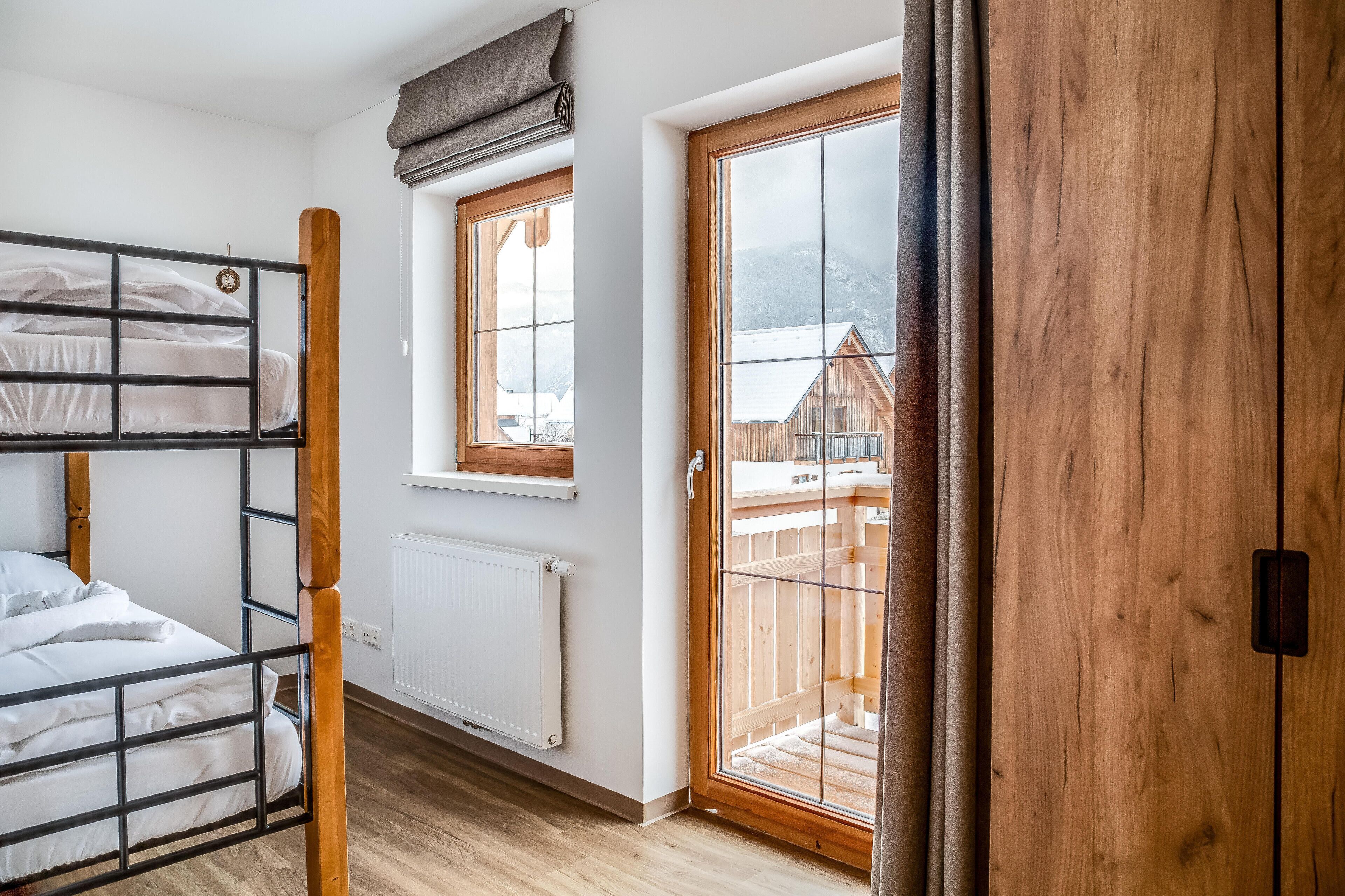 A room with bunk beds, a wooden door, and a window with a view of a building.