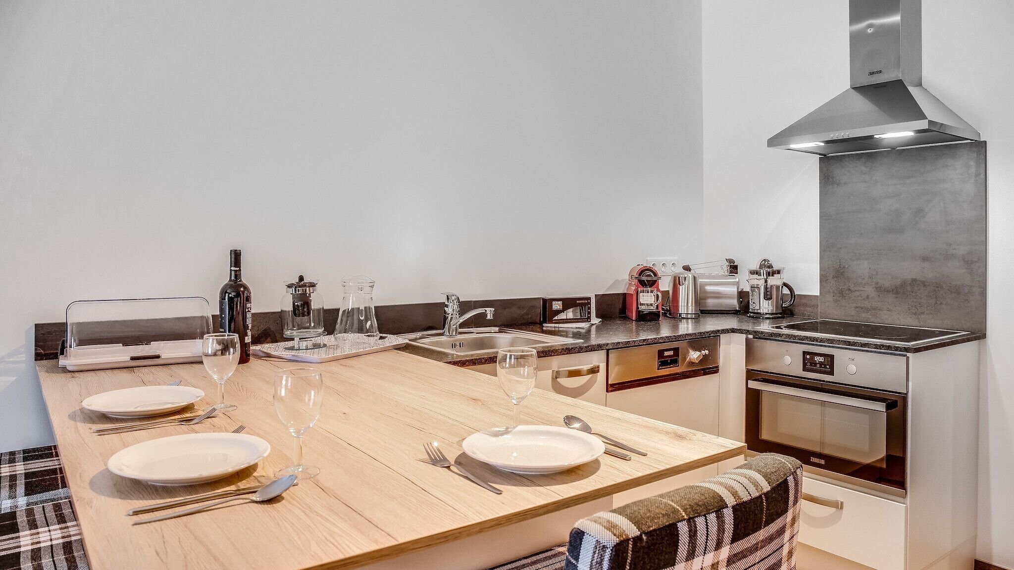A modern kitchen with a large dining table set for four, equipped with wine glasses and plates.