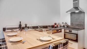 A modern kitchen with a large dining table set for four, equipped with wine glasses and plates.