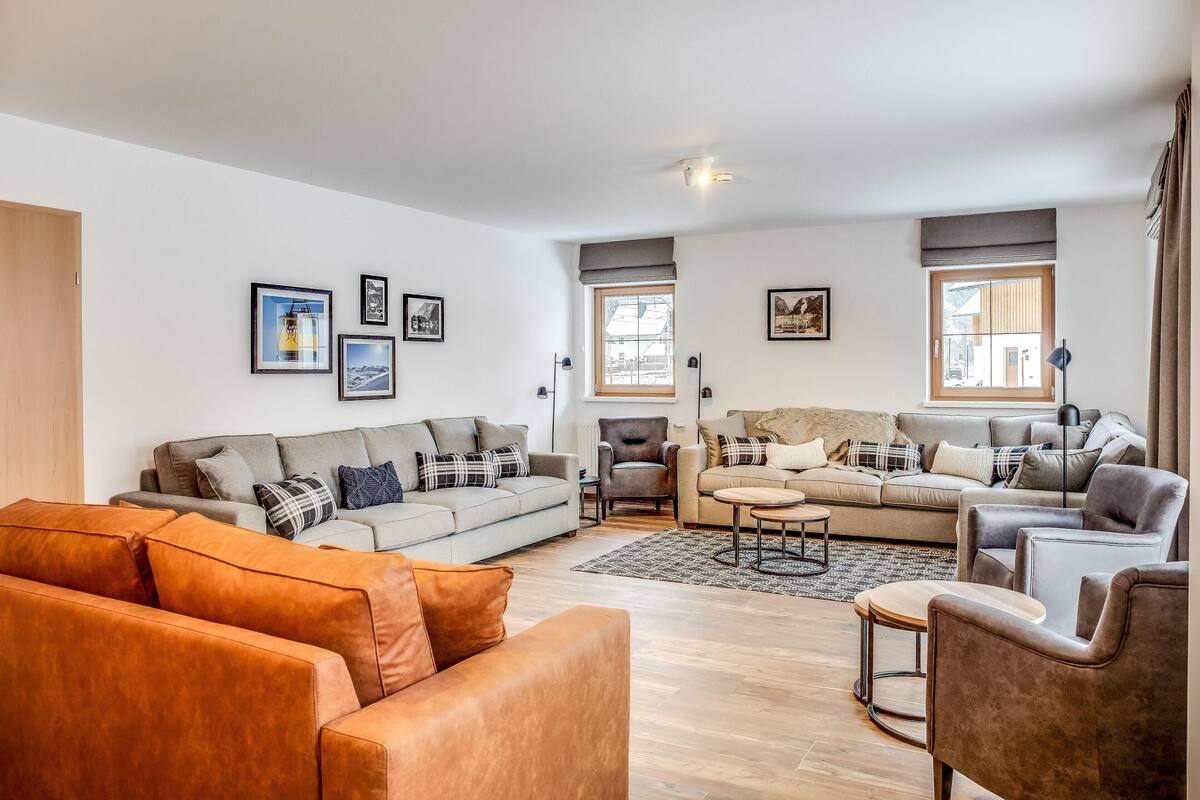 A modern living room with two sofas, a coffee table, and a side table. There are framed pictures on the wall and a window with curtains.