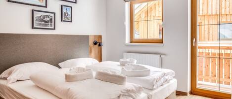 Ein Schlafzimmer mit einem großen Bett, einem Holzkopfende, einem Fenster mit Blick auf eine Holzterrasse und gerahmten Bildern an der Wand.