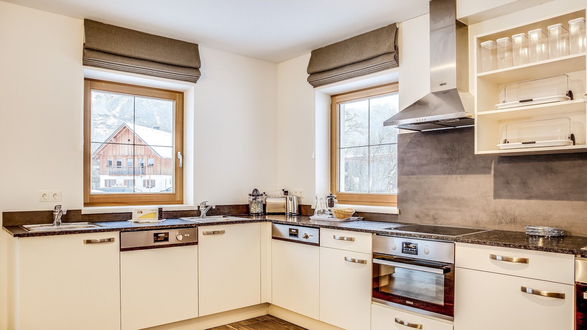 A modern kitchen with white cabinetry, a built-in oven, and a window with a view of a wooden house.