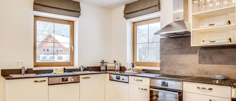 Una cocina moderna con armarios blancos, horno empotrado y ventana con vista a una casa de madera.