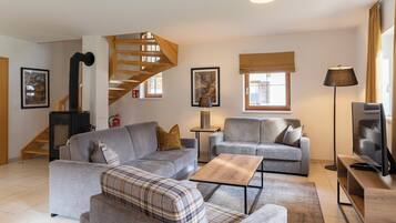 Una sala moderna con dos sofás grises, una mesa de centro de madera, un sillón escocés, un televisor y una escalera.