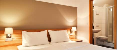 Habitación de hotel con cama, mesitas de noche y baño a la vista a través de una puerta abierta.