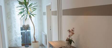 A hallway with a wooden floor, a reception desk, a potted plant, and a wall with a decorative panel.
