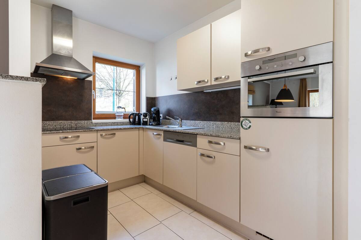 A modern kitchen with a built-in oven, stainless steel appliances, and a window providing natural light.