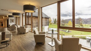 A spacious lounge area with multiple seating options, large windows offering a view of the outdoors, and a modern interior design. - Dormio Resort Obertraun (Obertraun)