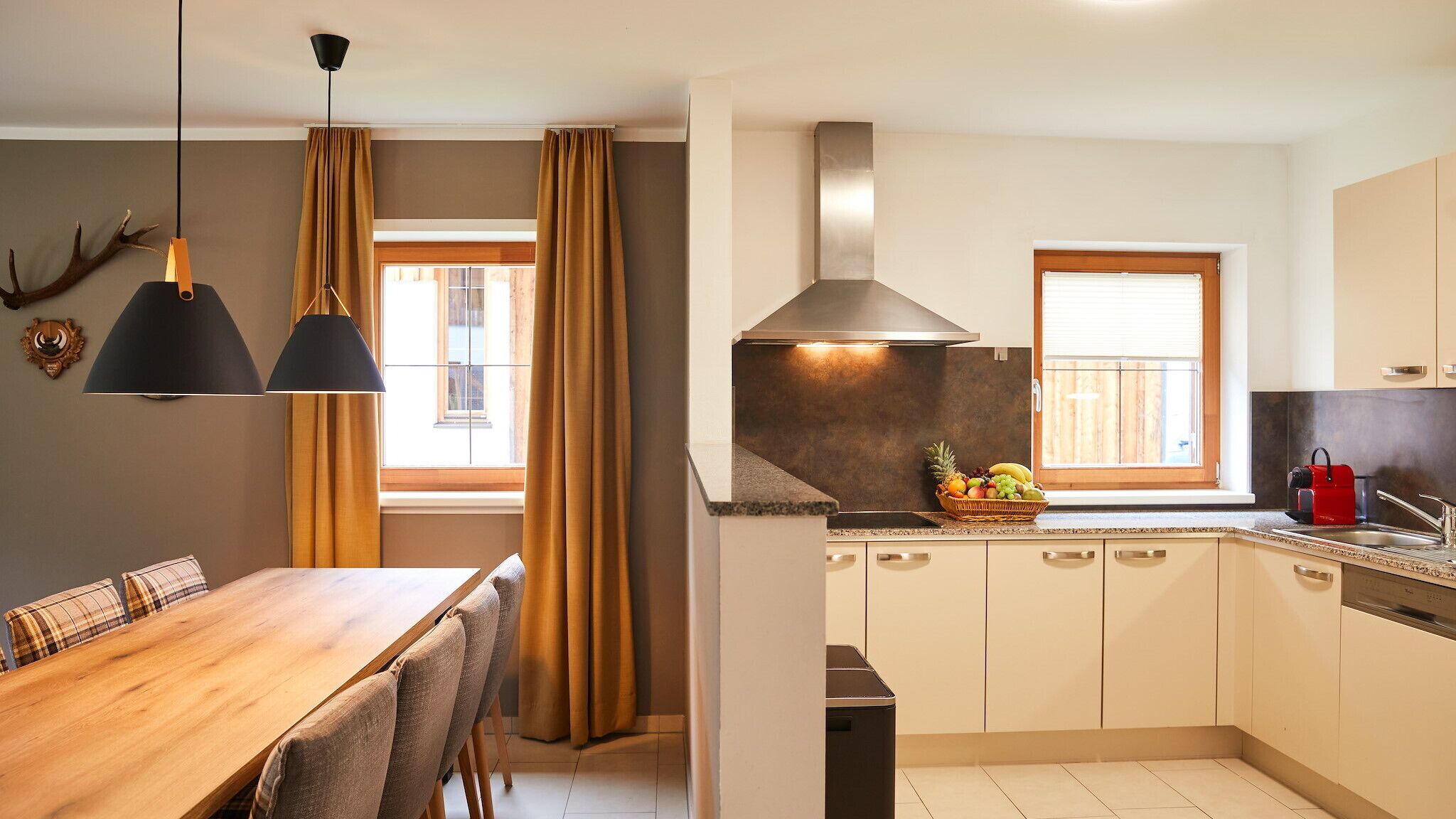 A modern kitchen with a dining area, featuring a wooden table and chairs, a built-in stove, and a fruit basket on the counter.