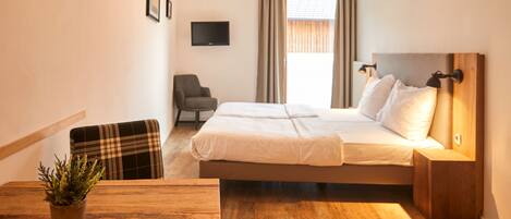 A hotel room with a bed, a chair, a TV, and a wooden table with a plant.