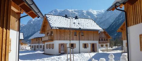 Una baita di legno con tetto innevato, circondata da neve e montagne.