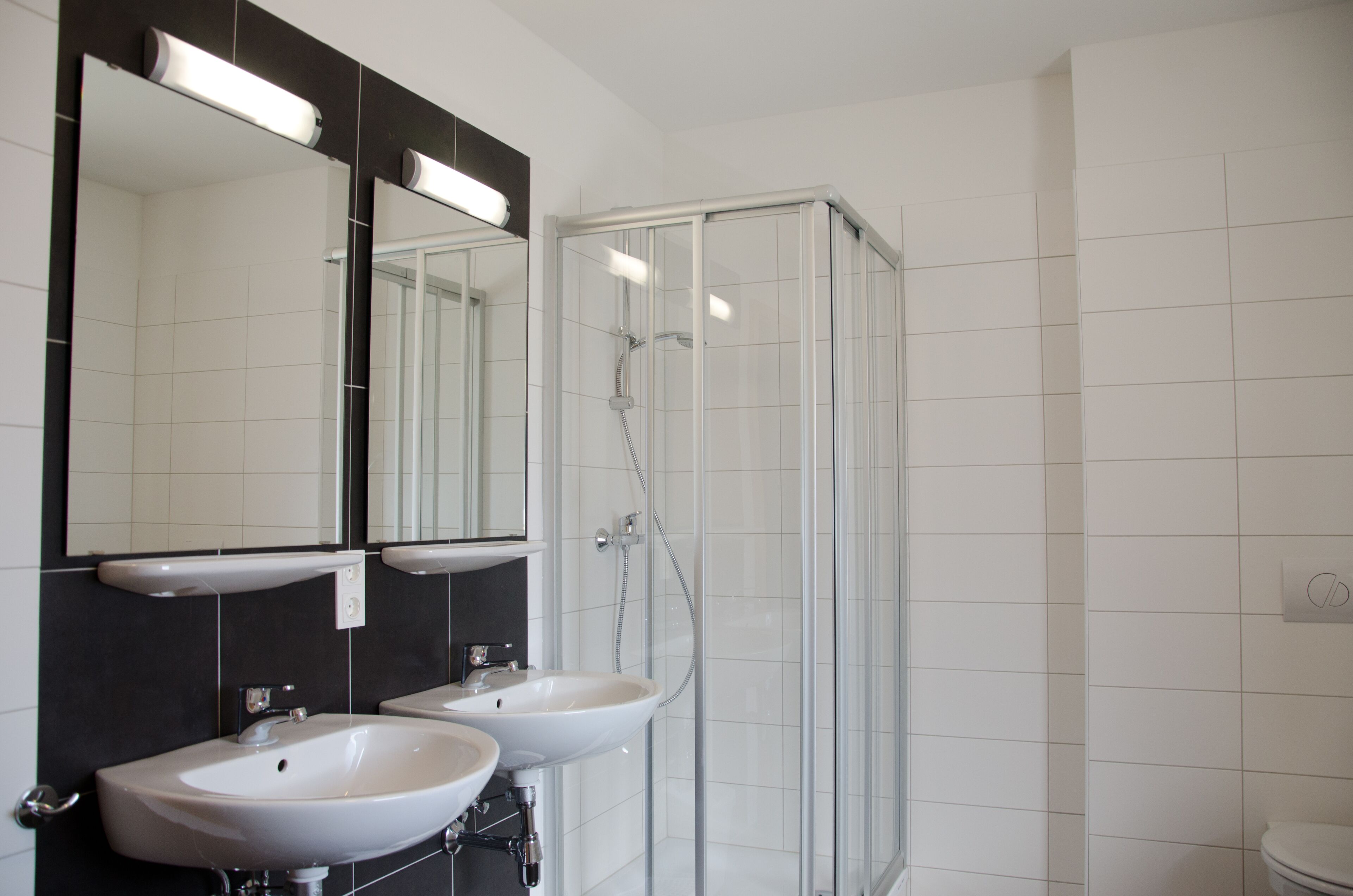 A bathroom with two sinks, a glass shower enclosure, and a large mirror with under-cabinet lighting.